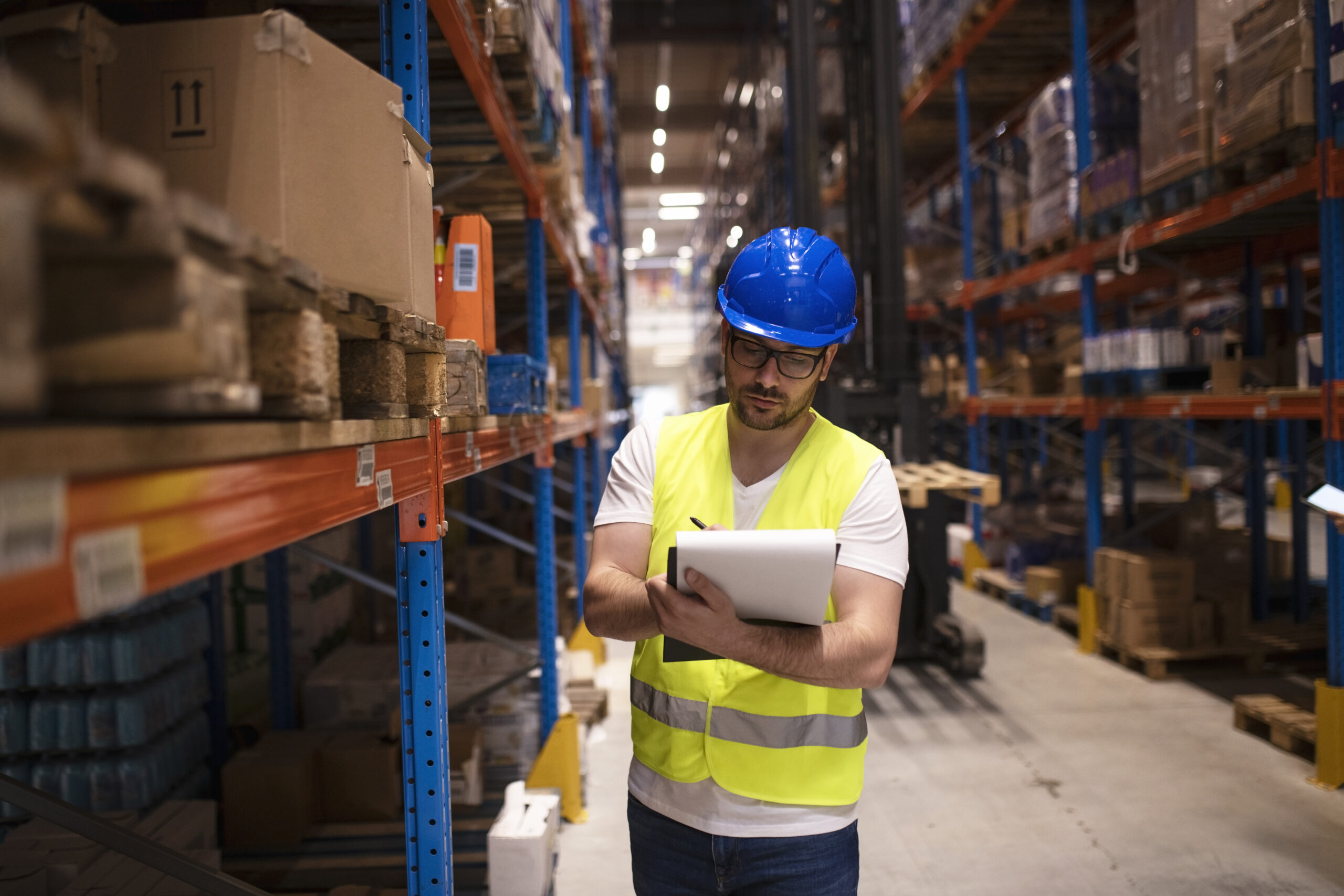 warehouse worker writing down inventory report on products in large storage area.